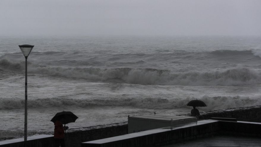 Varias personas se protegen con paraguas junto a la playa de la Zurriola de San Sebastián. El estado de la mar en aguas costeras del País Vasco será de fuerte marejada, mar de fondo del noroeste con olas de 3 metros, que disminuirán a 2,5 al final del día, y viento del noroeste de fuerza 5.