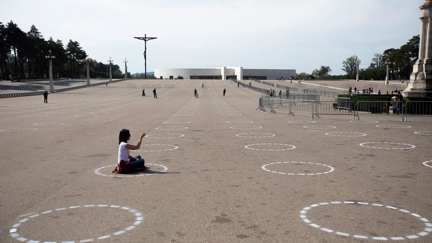Una peregrina sentada en uno de los círculos dibujados para delimitar la distancia de seguridad entre los fieles en la explanada del Santurario de Fátima, en Ourem, Portugal. 