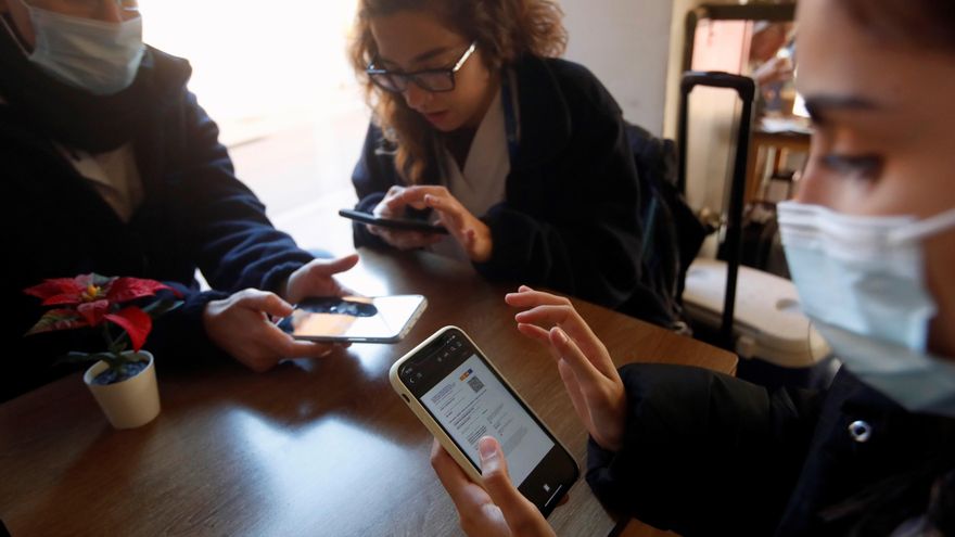 Tres personas preparan sus códigos QR del certificado de vacunación al entrar en un bar del barrio de Gracia de Barcelona, este viernes