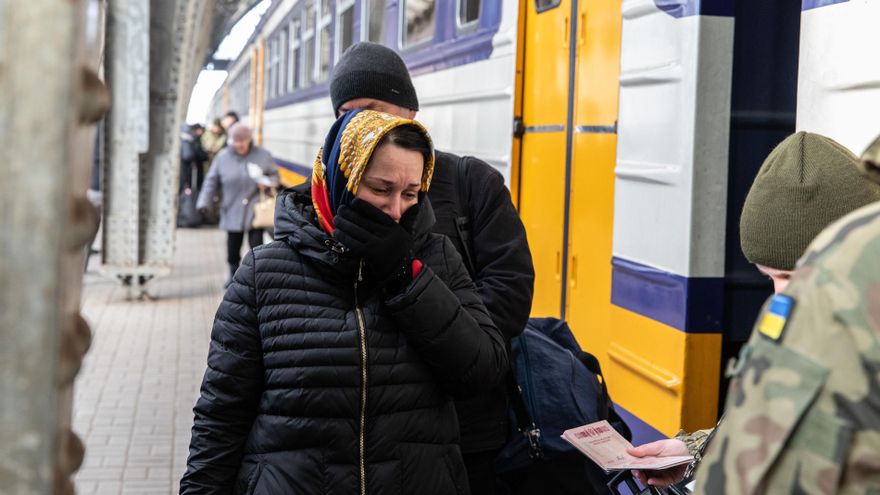 Una mujer espera mientras los soldados ucranianos comprueban su pasaporte antes de subir al tren hacia Polonia.