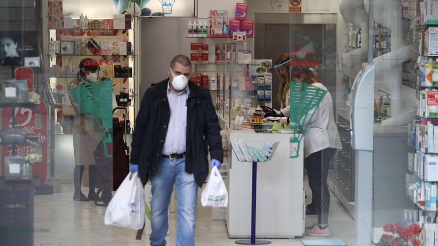 Un hombre protegido con mascarilla y guantes sale de una Farmacia