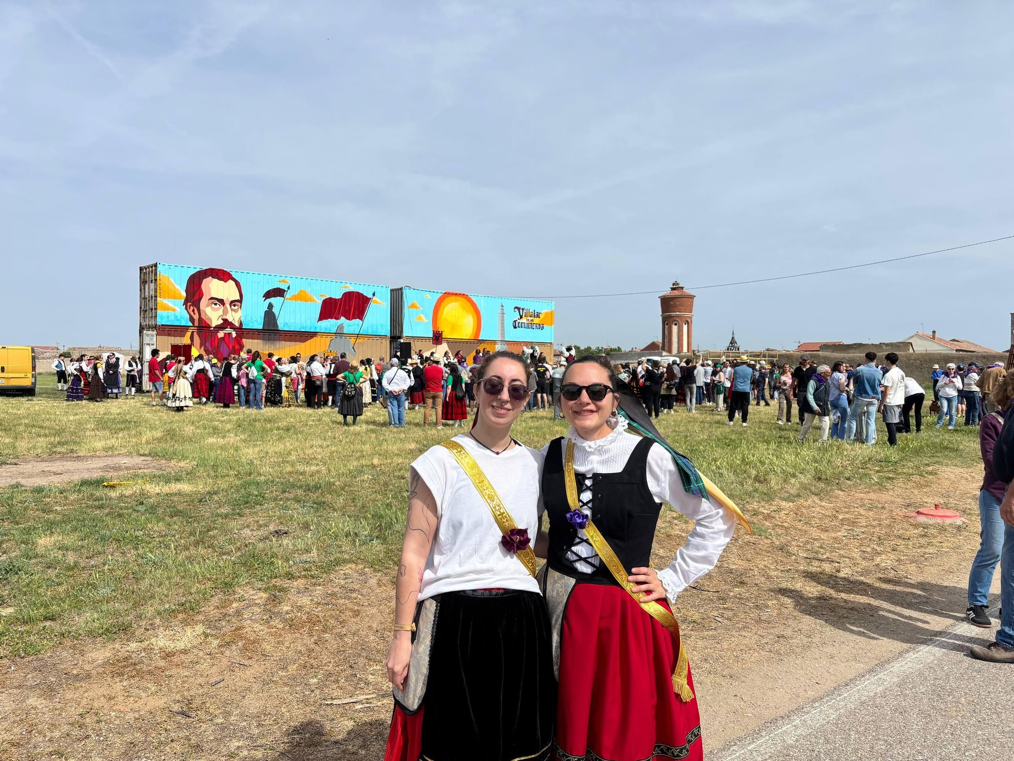 Lucía y Virginia posan junto al escenario en el que grupos tradicionales bailan.