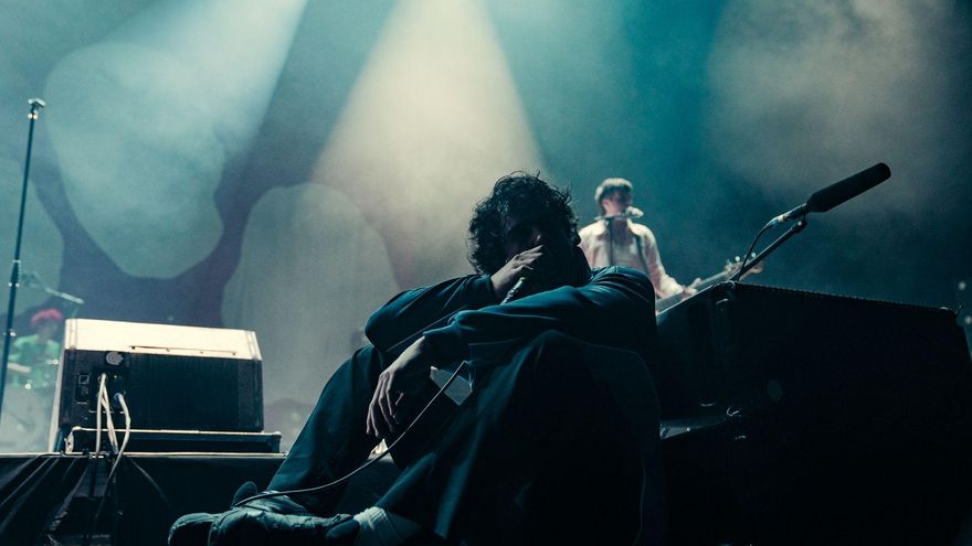 Diego Ibáñez canta desde el suelo del escenario, con el batería Juan Pedrayes y el bajista Martín Vallhonrat al fondo.