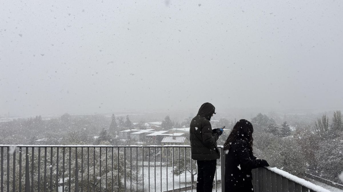 Dos personas toman fotografías de Pamplona cubierta de nieve.