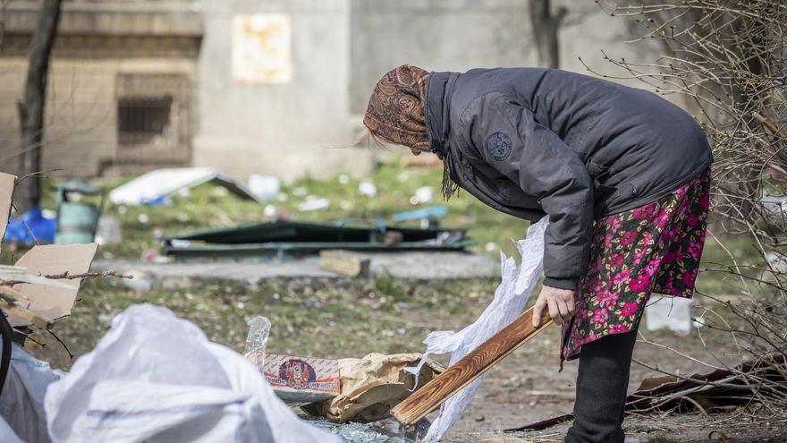Una mujer recoge restos cerca de un bloque de apartamentos destruido en Kiev