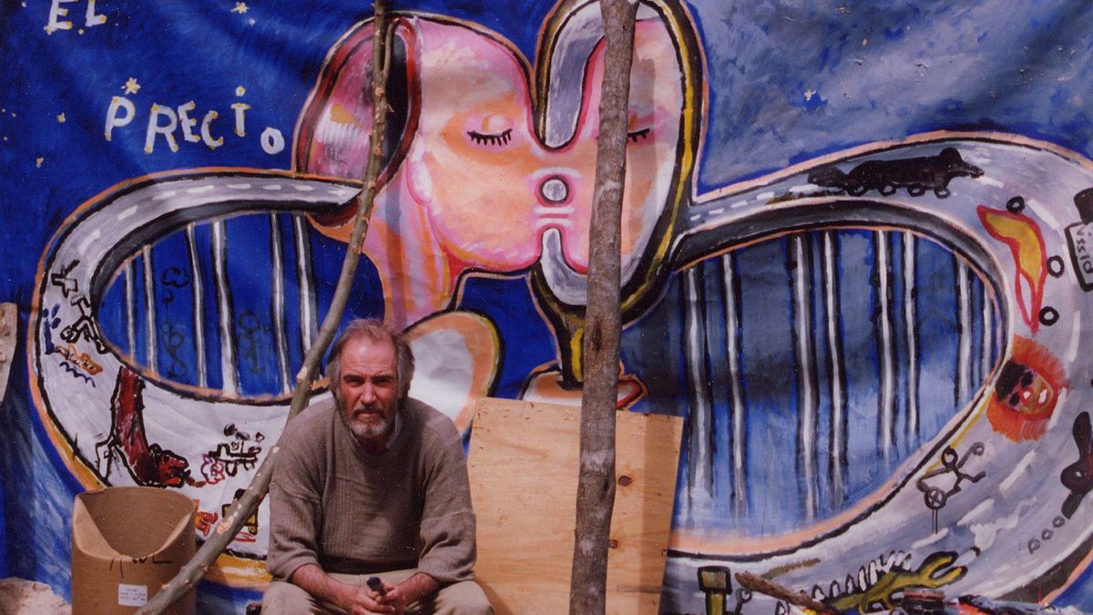 Mati Klarwein frente a una pancarta contra la autopista de la Tramuntana, años 90. El artista posa ante una de sus intervenciones públicas, realizada como parte de la campaña ciudadana contra la reforma de la carretera entre Deià y Sóller. La obra, titulada 'El precio del Progreso', estuvo colgada durante semanas en la avenida Argentina de Palma.