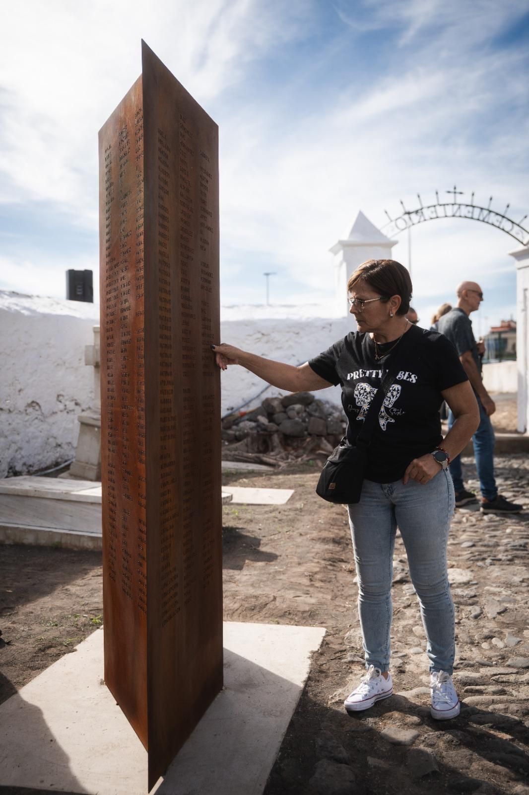 Una vecina lee los nombres de los difuntos en esta estructura colocada tras la rehabilitación del camposanto.