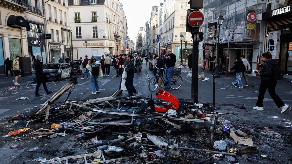 Unas personas pasan junto a los restos de una hoguera callejera tras los enfrentamientos entre la policía antidisturbios y los manifestantes en París. 