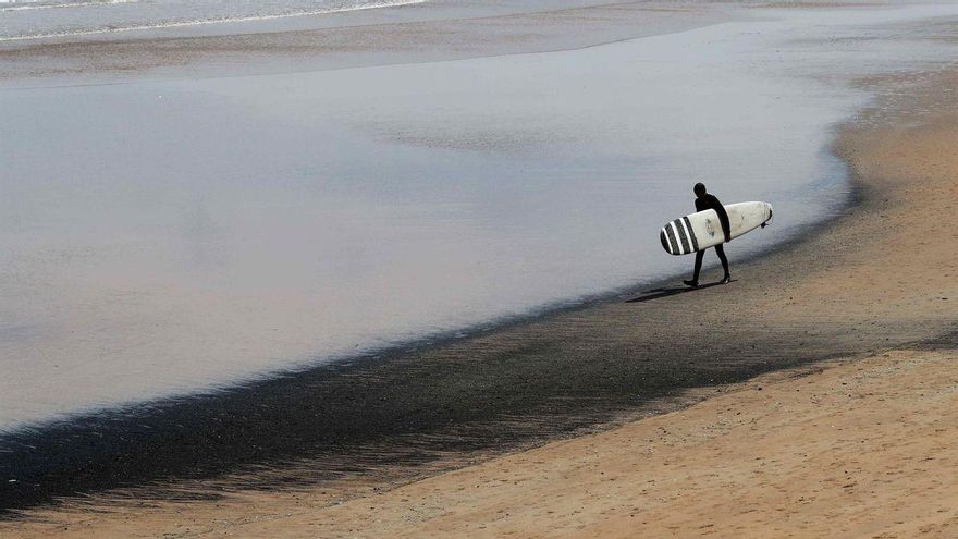Un surfista transporta su tabla en la playa de San Lorenzo de Gijón, este lunes.