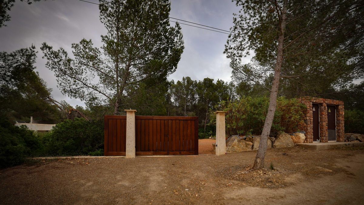 Una de las mansiones, en un entorno rural con pinos y arbustos, cuyo acceso está delimitado por un portón de madera.