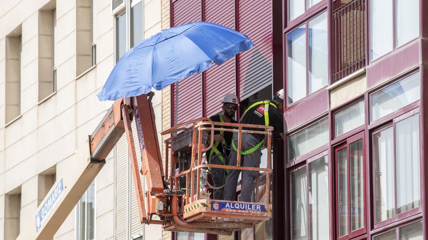 Dos operarios se protegen del sol mientras trabajan subido en una grúa en Murcia. EFE/Marcial Guillén