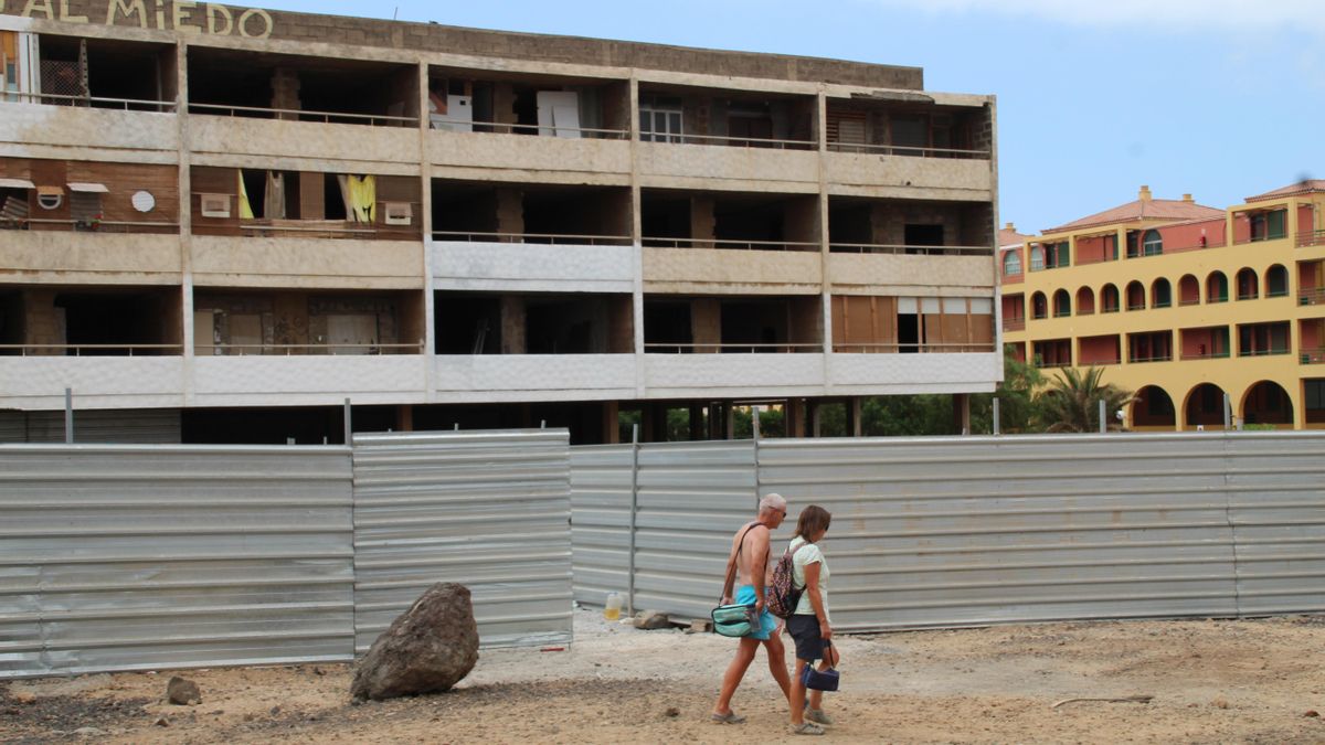 Dos personas caminan frente al edificio, vallado desde hace meses.