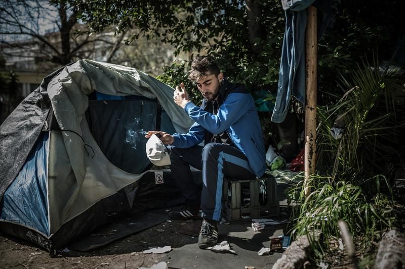 Mohamed (23 años), de Argelia. “Intenté ir a Europa por vías legales”. Duerme desde hace casi un mes en una tienda de campaña en Atenas, en un parque concurrido por drogadictos cerca de la plaza Victoria, donde acuden la mayoría de personas refugiadas y migrantes que llegan a la capital griega y que no tienen recursos para seguir su camino. Entre ellos, hay muchos jóvenes como Mohamed, procedentes de Argelia. “Yo quiero mi país, pero no su gobierno”, sentencia. Su nacionalidad es una de las muchas que tienen prohibido cruzar Macedonia, Serbia y Croacia y Eslovenia, paso imprescindible para llegar a Francia, donde le espera su novia, hija de padre argelino y madre francesa, que actualmente está estudiando en París. Intentó llegar a Europa por vías legales, pidió el visado para España y para Francia, pero en ambos casos se lo denegaron. Entonces decidió llegar por vías más peligrosas, como cruzar el mar. Ya en Grecia intentó cruzar la frontera con Macedonia con papeles falsos, pero le devolvieron a Atenas. Le han dicho que por 2.000 euros podría esconderse en un tractor que lo llevaría a Alemania, pero él no tiene tanto dinero. Habla regularmente con sus padres y les miente: “Digo que estoy bien, no quiero que se preocupen por mí”, asegura este chico que consigue comer caliente y ducharse regularmente en un centro de Cáritas que da apoyo a jóvenes como él. Ahora, lo que más miedo le da es que le coja la policía. “No quiero volver a Algeria, eso sería lo peor”. © Pablo Tosco/Oxfam Intermón