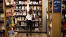 Una mujer alcanza un libro en una estantería de una librería.