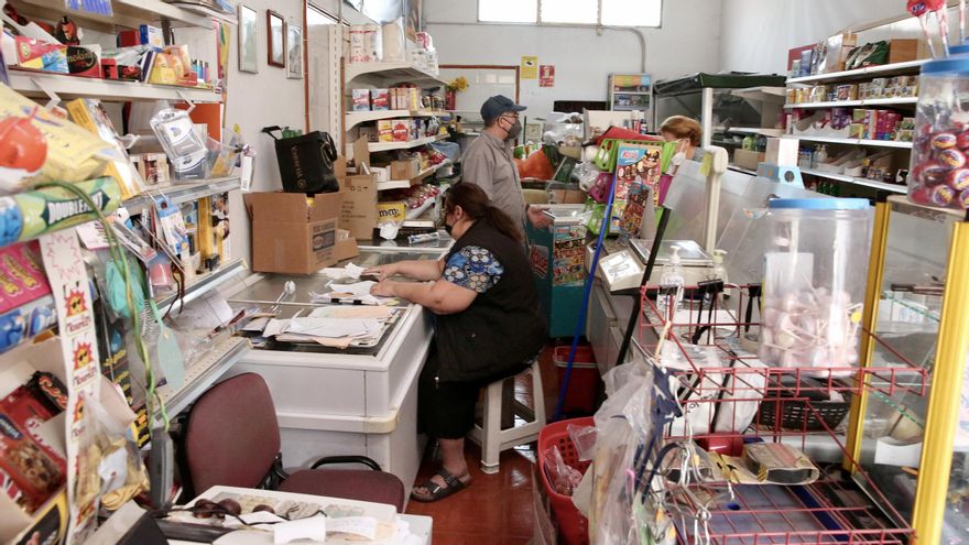 Carmen, sentada, revisando el inventario que debe vender o guardar. Pedro, a su vez, le recita qué hay y qué no en la tienda que temen perder si la lava avanza por el barrio de La Laguna