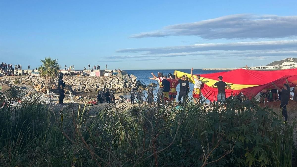 Manifestantes con una bandera gigante de España en una playa de Ceuta