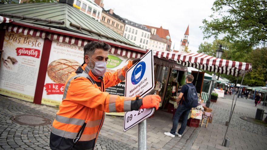 Un trabajador municipal coloca un cartel en el que se pide el uso de la mascarilla, en el centro de Munich, Alemania. 