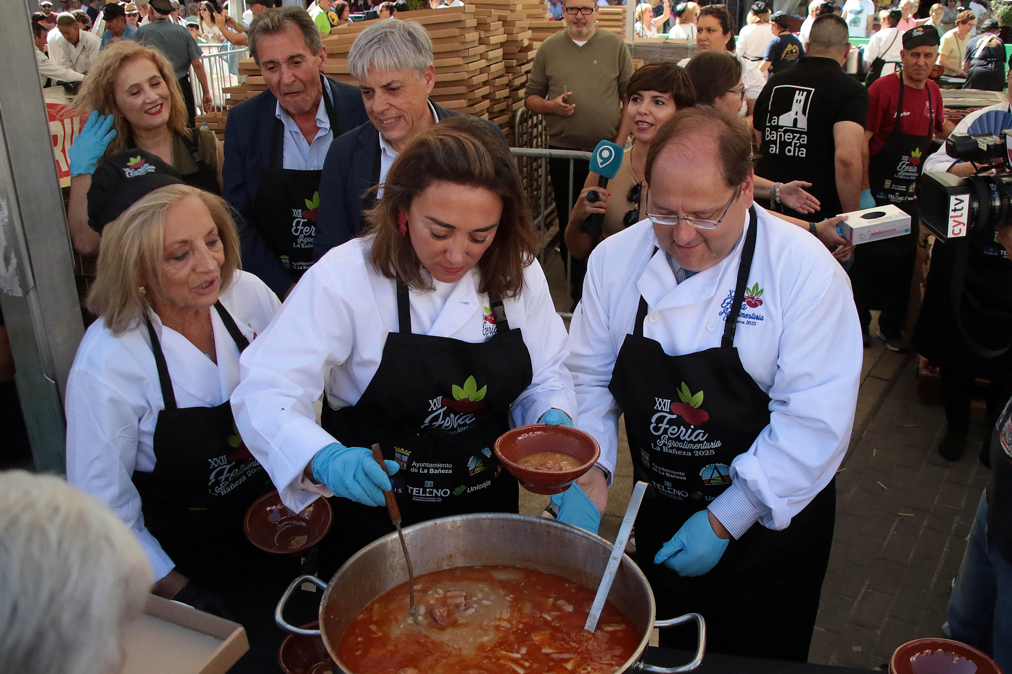 La consejera de Agricultura, María González Corral, sirve raciones de alubias junto al alcalde de La Bañeza, Javier Carrera.