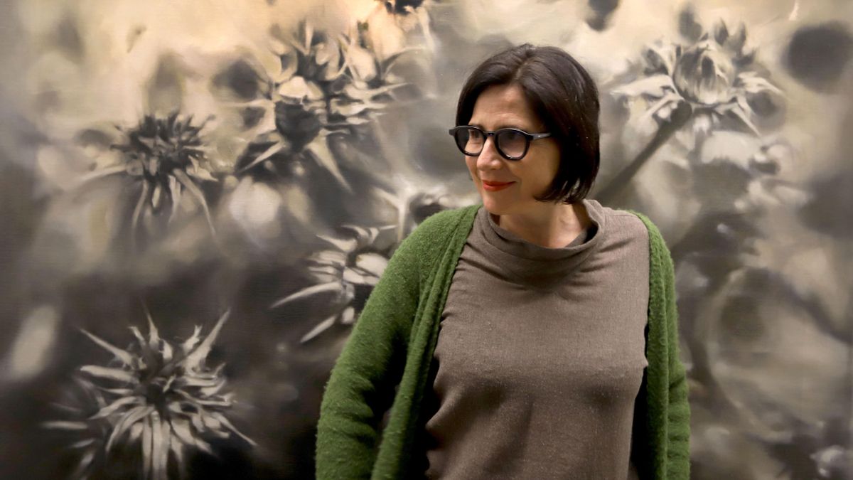 L’artista Mery Sales davant d’un dels seus quadres grans on la natura conversa amb la força de la fragilitat de María Zambrano i les flors fetes malbé.