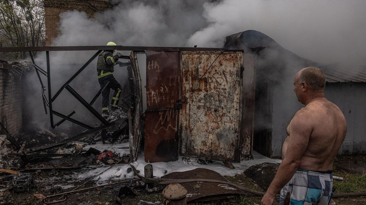 Kharkiv (Ukraine), 18/04/2022.- A man looks at a firefighter trying to extinguish the fire in burning garages that were hit by Russian artillery shelling, in Kharkiv, northeast Ukraine, 18 April 2022. Kharkiv and its surrounding areas have been heavily shelled by Russian forces, causing many civilians deaths, since the invasion of Ukraine which began on 24 February. (Incendio, Rusia, Ucrania)
