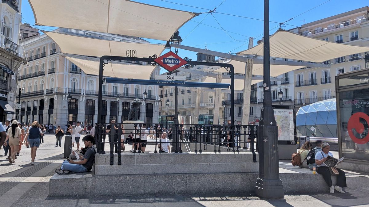 Viandantes sentados en los bancos bajo la sombra de la Puerta del Sol