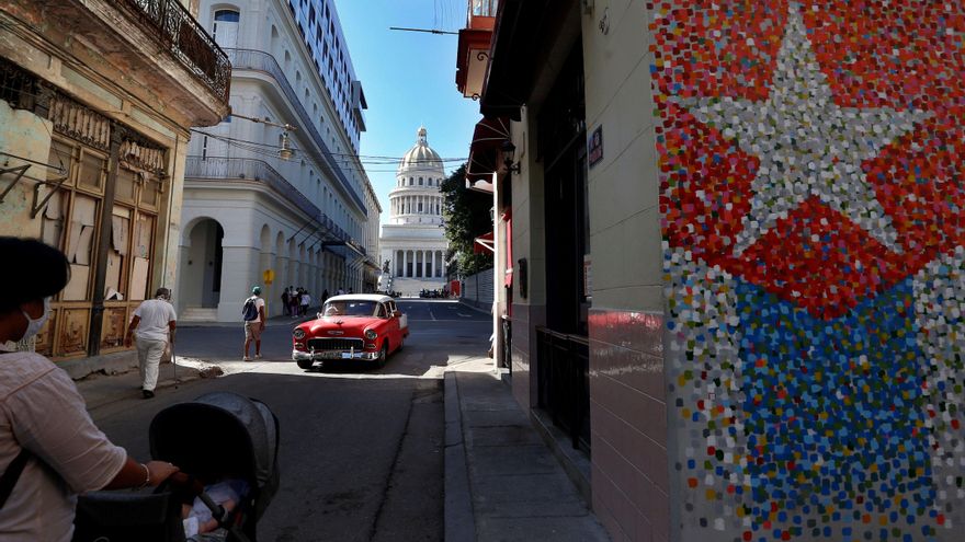 Un vehículo clásico y varios peatones pasan hoy por una calle con murales de la bandera cubana, junto al Capitolio en La Habana (Cuba). EFE/ Ernesto Mastrascusa