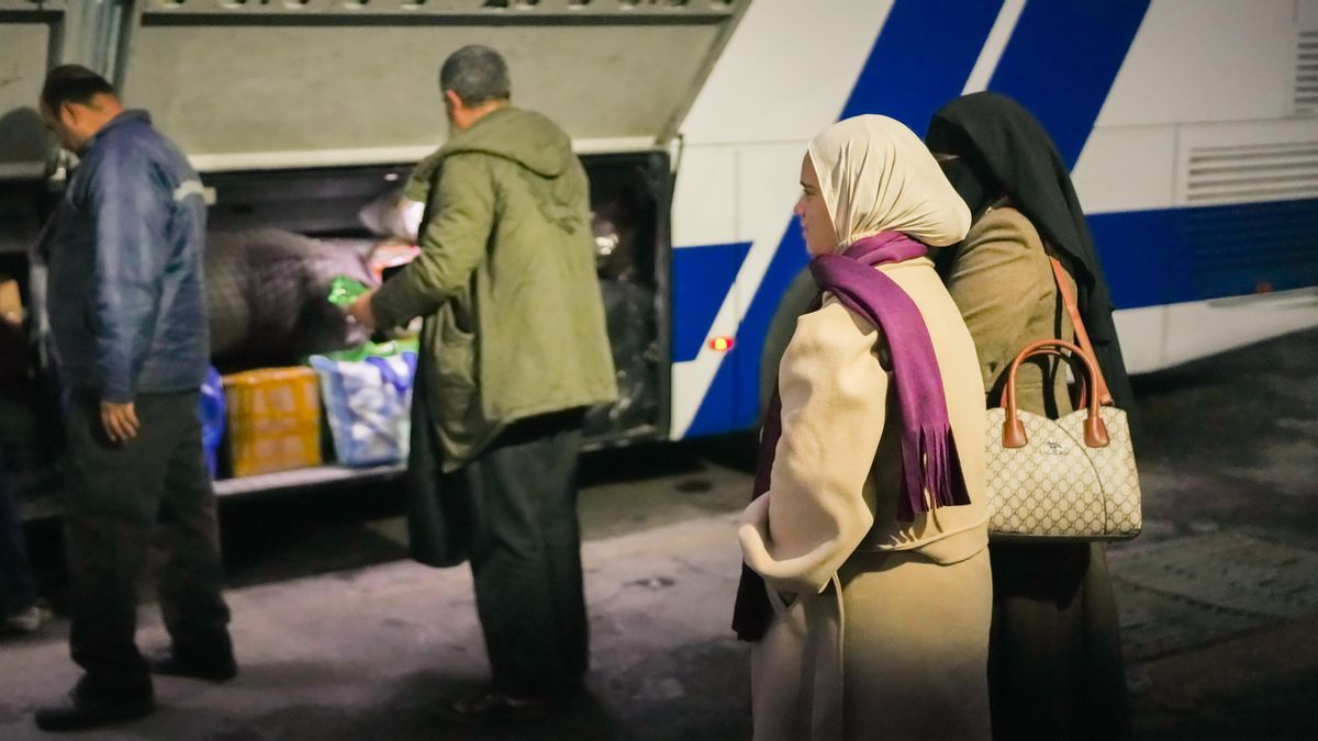 Mona y su hija Maya miran como los operarios meten las maletas dentro del bus que les llevará a Siria