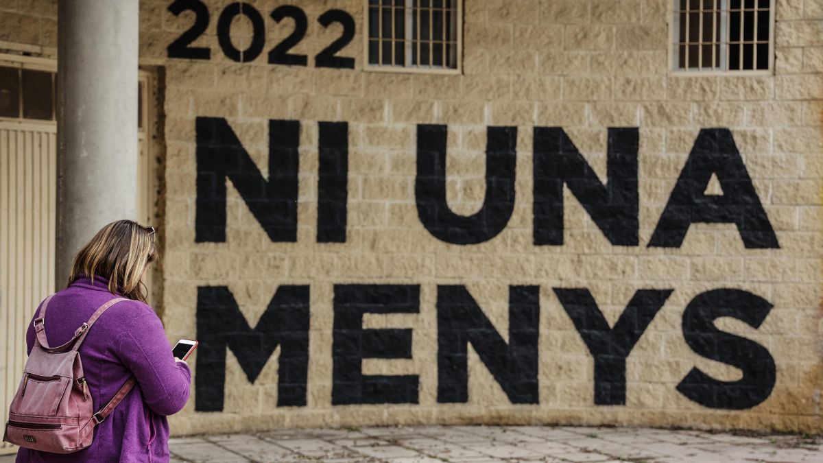 Una mujer pasa por delante de una pared donde se puede leer "Ni una menos" en un acto en memoria de las víctimas de violencia de género y sus hijas e hijos, en el antiguo cauce del Turia, a 8 de marzo de 2022, en Valencia, Comunidad Valenciana (España)