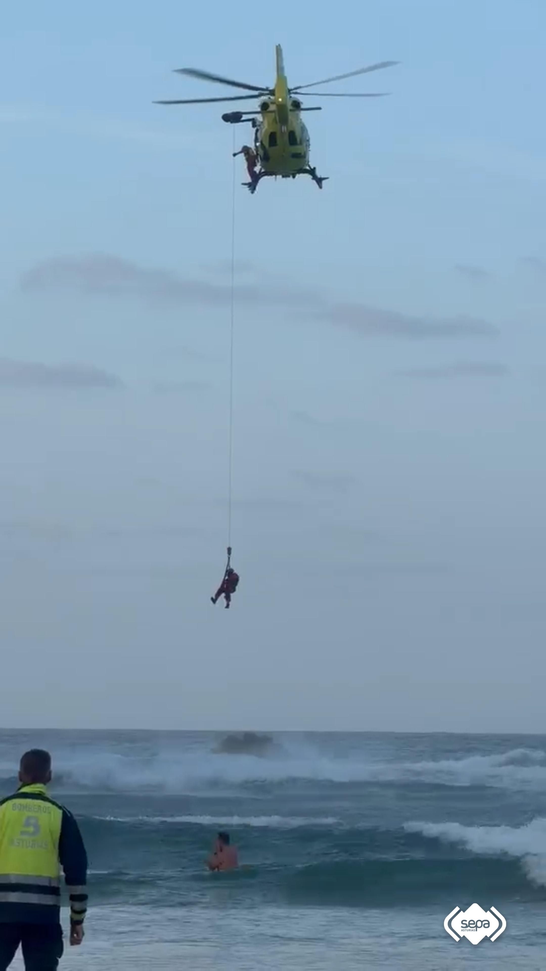 El helicóptero durante las labores de evacuación de los bañistas que se encontraban en apuros para salir del agua en la playa de La Franca, en Asturias, por el fuerte oleaje.