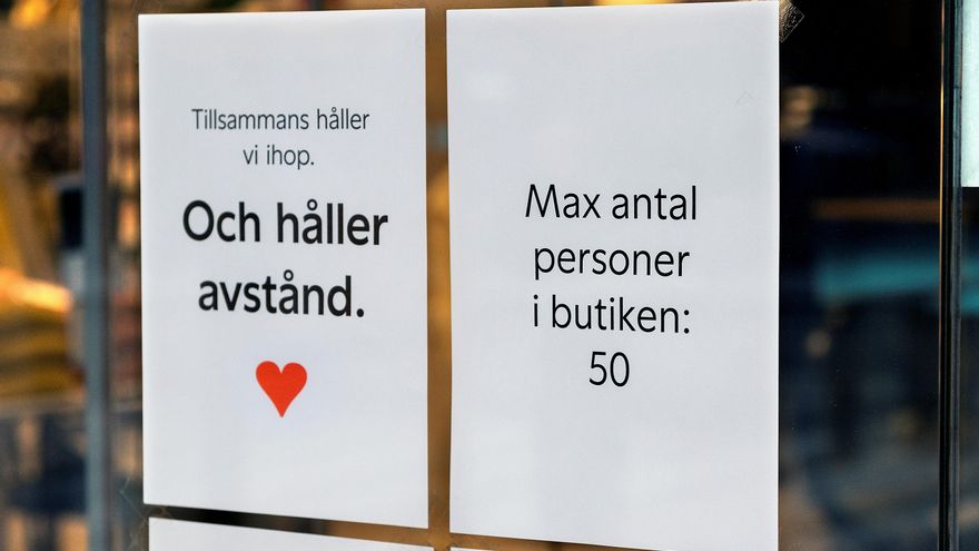 Dos carteles que dicen 'Mantener la distancia' (i) y 'Número máximo de personas en la tienda 50' (d) cuelgan del escaparate de una tienda en Estocolmo, Suecia. EFE / EPA /Archivo