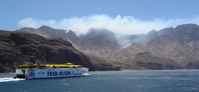 El ferry de Fred Olsen sale del puerto de Las Nieves, en Agete, mientras en lo alto del acantilado sigue activo el foco del incendio de Gran Canaria en el pinar de Tamadaba. EFE/Elvira Urquijo A.