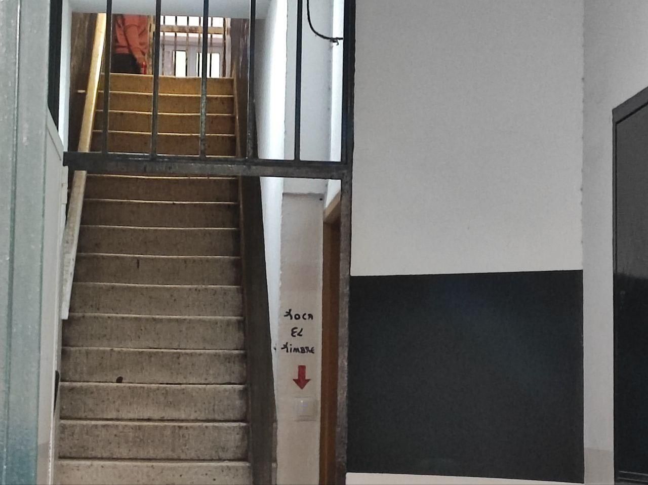 Un hombre sostiene una cerveza en el interior del bloque, con una señal y la frase "toca el timbre" en la entrada del portal".