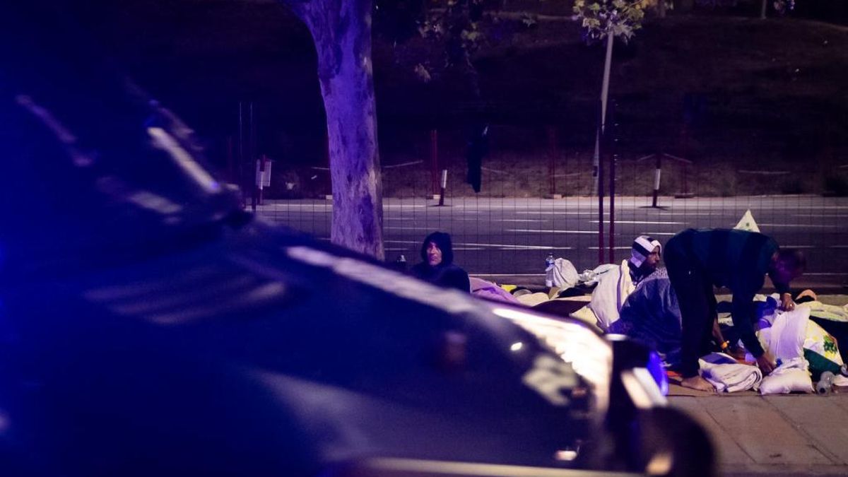 Migrantes que dormían en las calles colindantes al embolsamiento de Loma Colmenar se despiertan ante la llegada de varios furgones de la Policía Nacional.