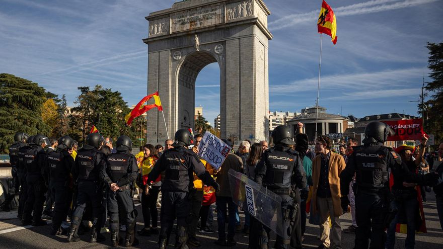 Unos jóvenes sostienen banderas y pancartas frente a efectivos de la Policía Nacional durante la manifestación que han trasladado hasta las inmediaciones de La Moncloa y los accesos de la A-6 a la capital, este sábado.