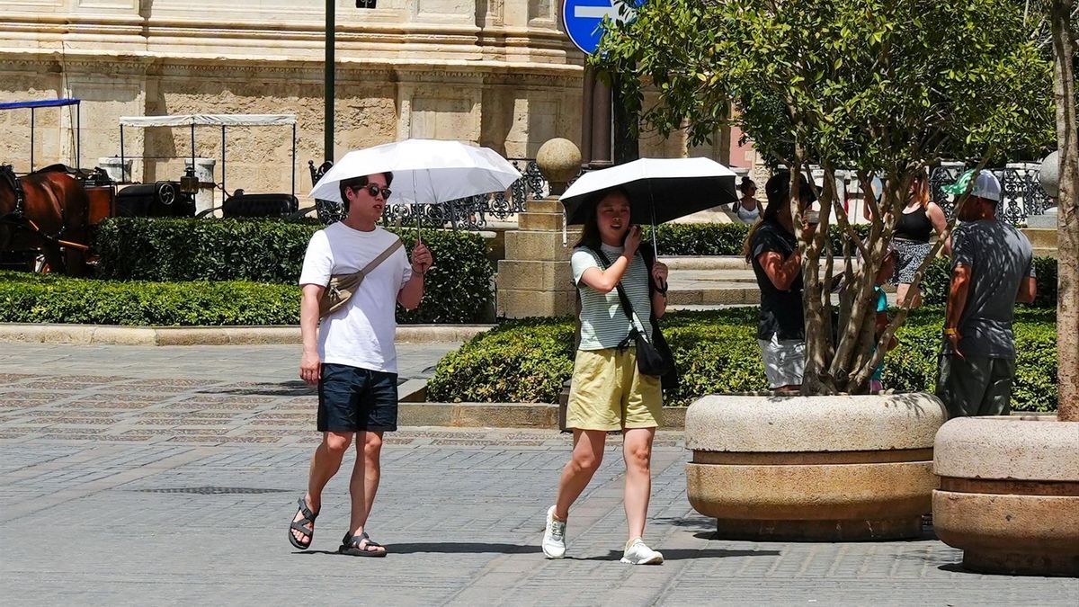 Dos turistas se protegen del sol con una sombrilla en el centro de Sevilla.