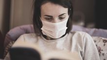 Una mujer con mascarilla mientras lee un libro