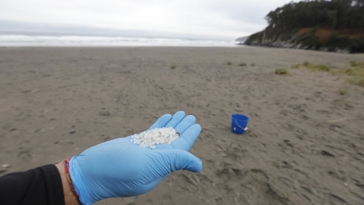 Archivo - Un operario de TRAGSA coge con la mano pellets de plástico en una playa asturiana