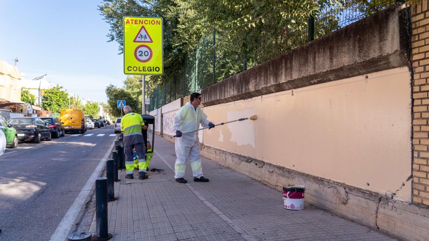 Operarios limpian el muro de un colegio en Sevilla.