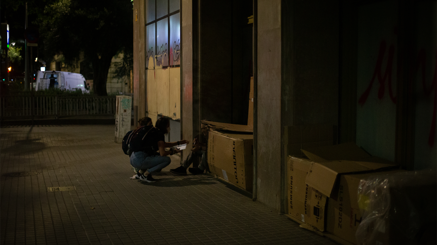 Una voluntaria habla con personas que duermen en cajas de cartón.