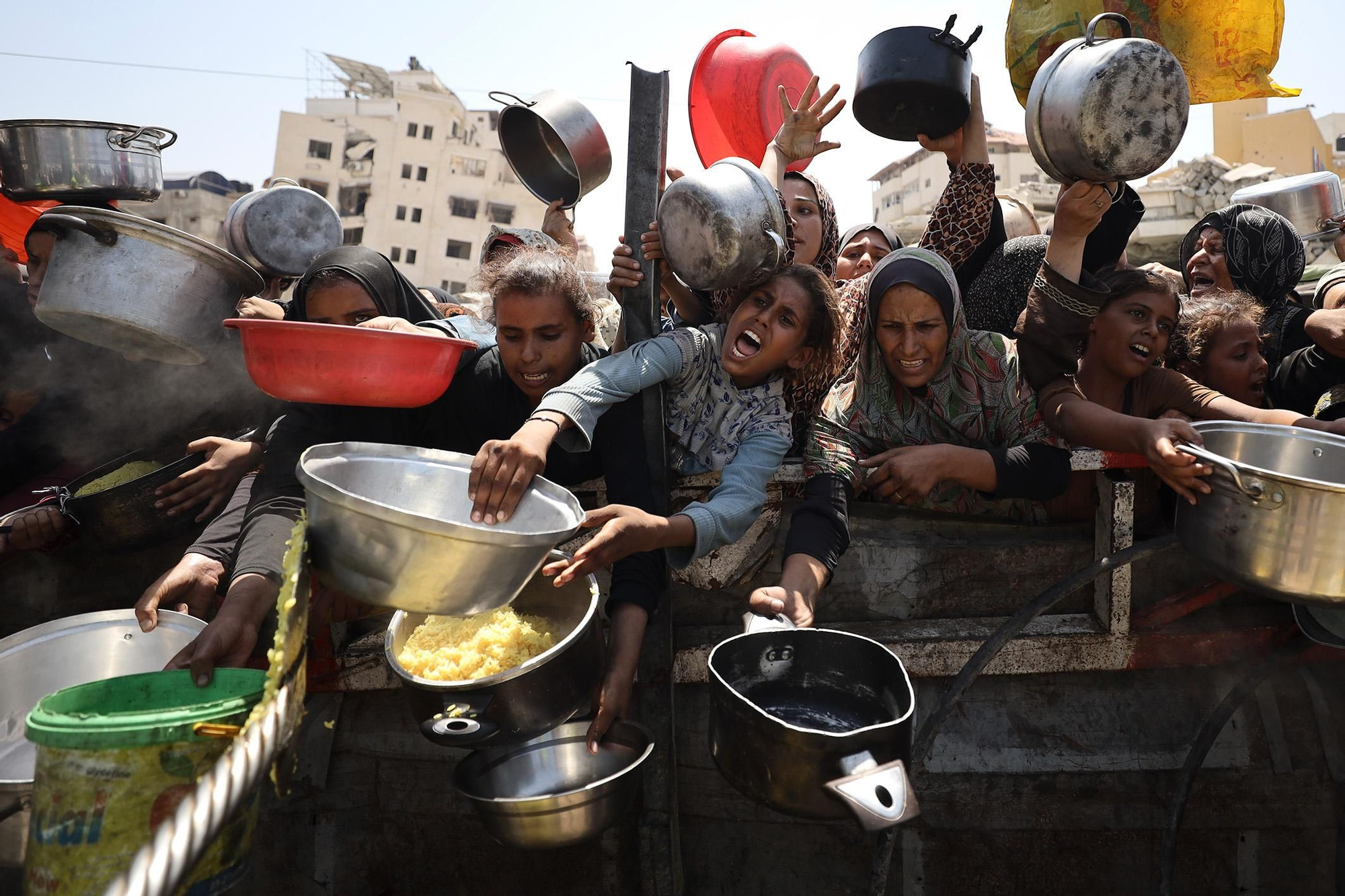 En una escena que se repite a diario en los puntos de distribución de Gaza, una multitud de mujeres y niños se agolpa y avanza, levantando sus recipientes con la esperanza de recibir una comida. 24 de agosto de 2025. © Khames Alrefi. Ganador del Premio Visa d’Or Humanitario 2026 del Comité Internacional de la Cruz Roja (CICR).