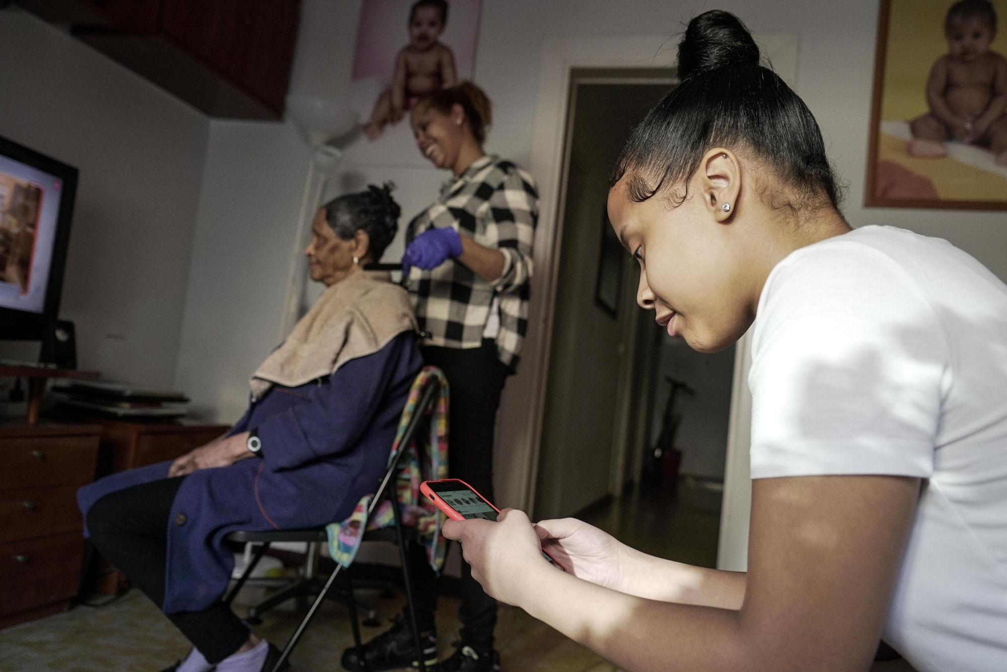 Vanessa Medina (16 años) consulta el móvil mientras su madre le arregla el pelo a su abuela en el salón de su casa, situada en el distrito de Nou Barris de Barcelona.