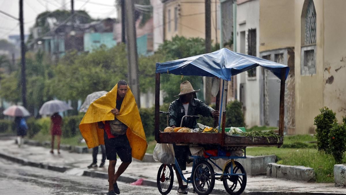 Personas se protegen de la lluvia este martes, en Santiago de Cuba (Cuba).