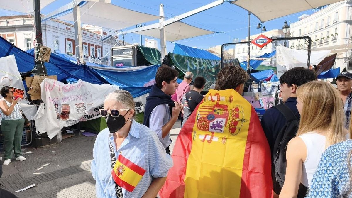 Varias personas con banderas de España pasan por la Puerta del Sol