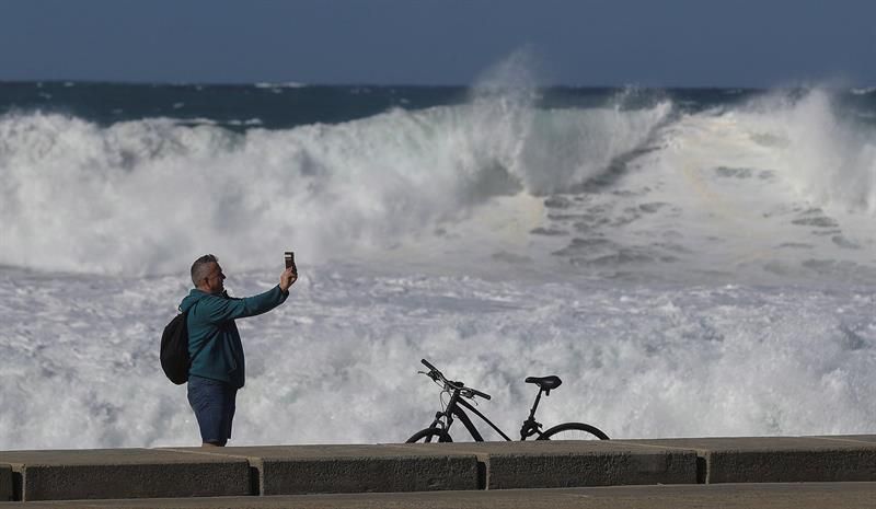 Un hombre se toma fotografías con el oleaje de fondo en el paseo de la playa de Las Canteras en Las Palmas de Gran Canaria. EFE/Elvira Urquijo A.