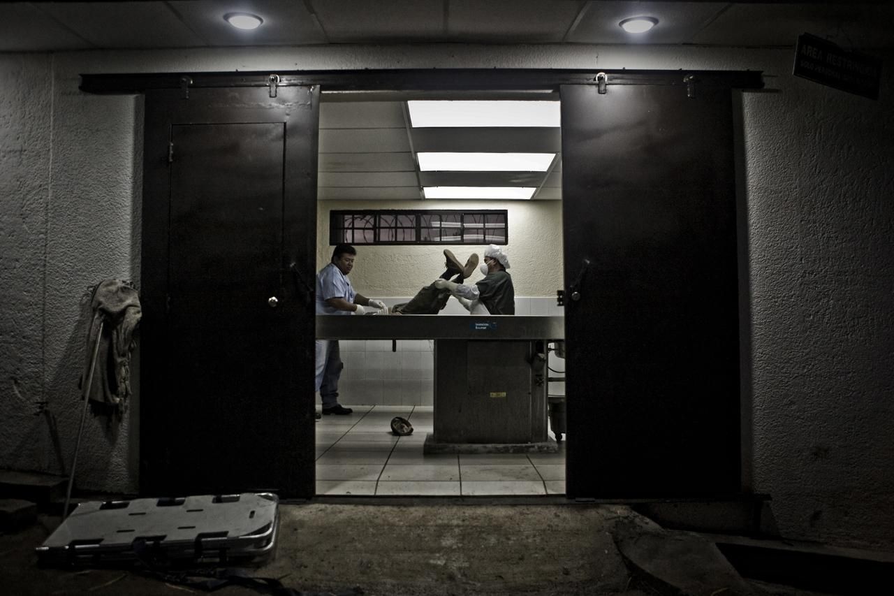Dos empleados de Medicina Legal mueven un cadáver en la sala de autopsias para iniciar la inspección postmortem. /Edu Ponces (RUIDO Photo)