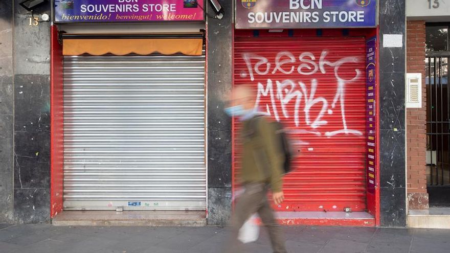 Un vecino pasa ante una tienda de recuerdos con la persiana bajada en un comercio cercano al Camp Nou