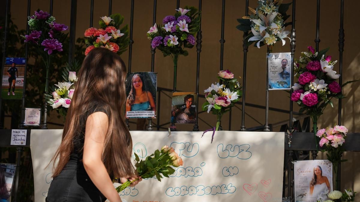 Una joven pasa junto al altar en memoria de Sandra Peña, que ha sido repuesto en las rejas del bloque de viviendas de la calle Rafael Laffón.