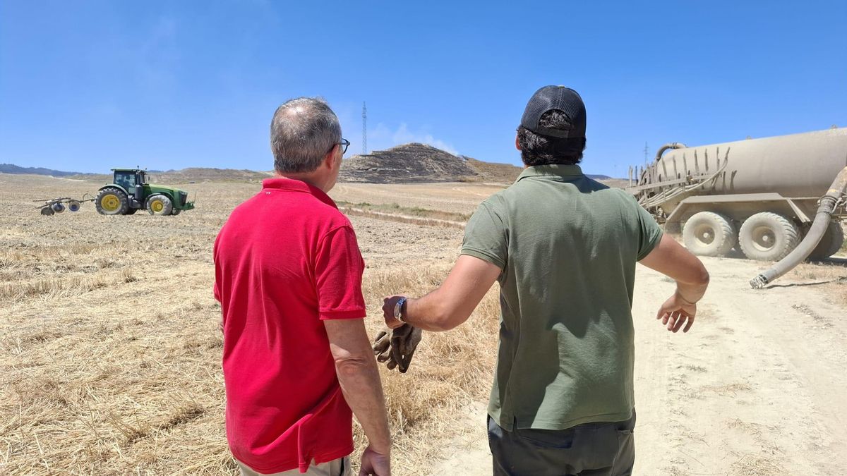 Juan Carlos Borrell, a la derecha, junto a un vecino de Robres tras ayudar a frenar la extensión del fuego en la loma que se observa al fondo.