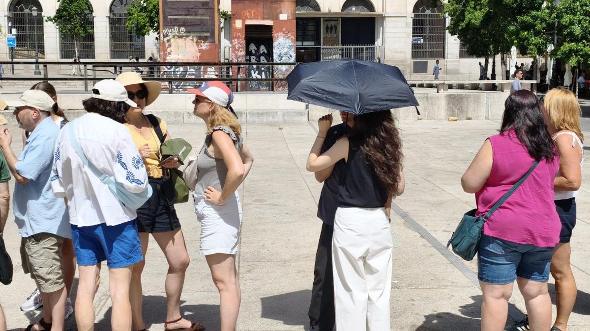 Varias personas se protegen del sol mientras esperan en una plaza de Madrid.