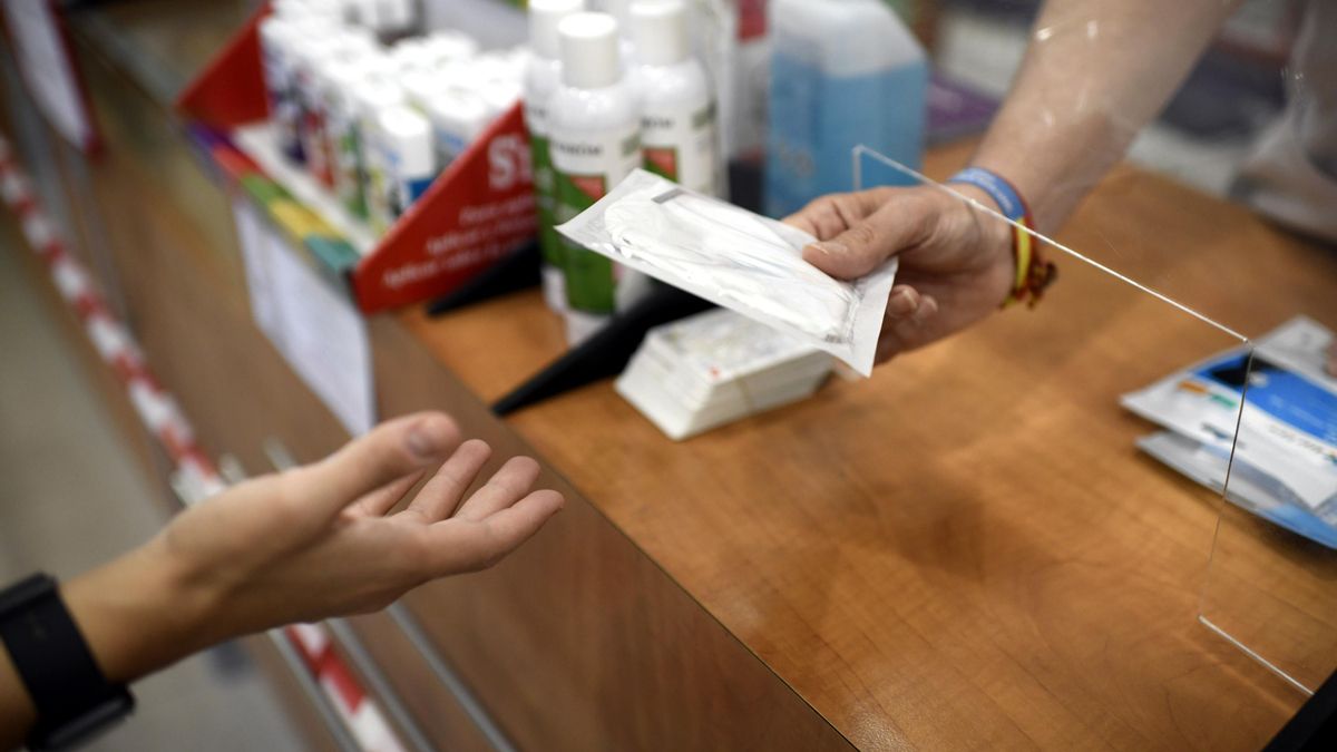 Un farmacéutico entrega a un cliente una mascarilla